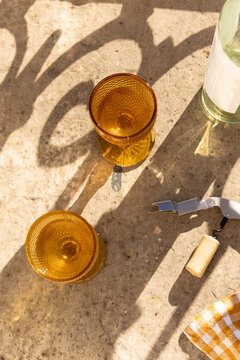 overhead shot of amber gold vintage goblet wine glass with bottle of white wine and wine opener with cork on concrete surface 