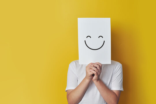 Boy Hiding Face Behind Smiley Card on a yellow background
