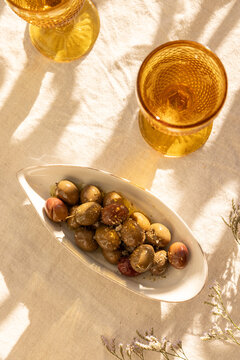 overhead shot of mustard gold wine glasses on linen tablecloth with ceramic handmade plate of olives garnished with salt and dried herbs with dappled shadows in afternoon light
