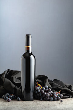 Bottle of red wine with grapes on a grey background.