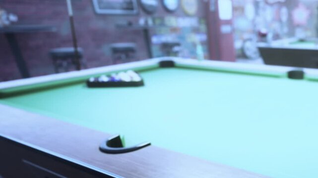 A group of friends plays pool at a bar during the weekend. The game takes place near the window, with a view of the street outside. The green table holds a set of billiard balls.