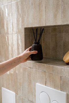 Modern tiled bathroom with hand placing aroma diffuser on shelf