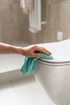Cleaning a toilet bowl in a restroom with a hand and cloth