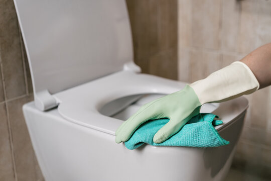 Cleaning the toilet bowl in a restroom with a green glove and cloth