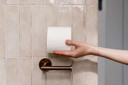 Woman holding fresh toilet paper roll near holder on tiled bathroom wall