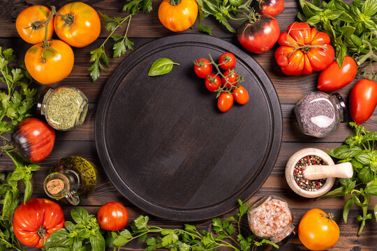 Fresh vegetables, herbs, spices, and olive oil surrounding a dark wood board