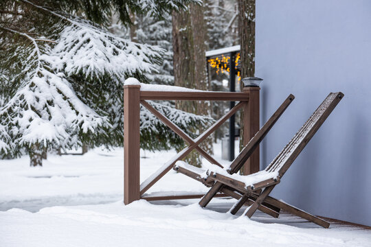 Two wooden deck chairs covered with snow on outdoor terrace in winter during daytime