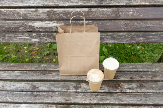 Paper takeaway bag and two coffee cups on wooden park bench