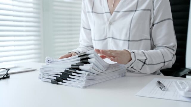 Accountant or financial professional reviewing business documents and calculating expenses on a white desk, managing taxes, financial records, and official paperwork for audit or reporting