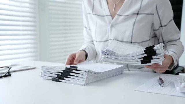 Accountant or financial professional reviewing business documents and calculating expenses on a white desk, managing taxes, financial records, and official paperwork for audit or reporting