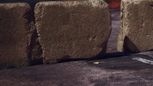 Two large stones are positioned closely together in a parking lot. The area is marked with white lines. The scene shows part of the asphalt surface and some slight debris.