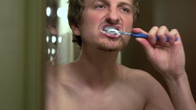 Male brushing teeth in bathroom close up
