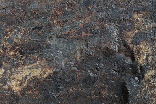 Gritty dark grey rock surface heavily textured with bright brown rust mineral deposits