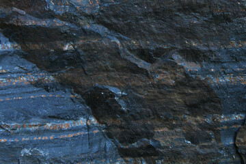 Horizontal layered dark slate rock texture with rusty mineral streaks © Valeri