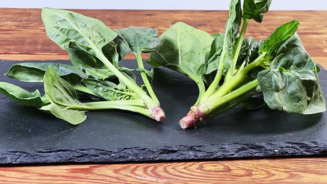 Fresh spinach stems on flat slate plate on rustic table