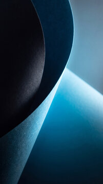 A high-contrast, minimalist abstract composition featuring soft curved layers of blue and dark paper with dramatic lighting and smooth gradients.