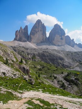Iconic Tre Cime di Lavaredo, three famous rocky peaks rising above the alpine valley on a sunny summer day. Popular loop hiking route and classic postcard symbol of the Dolomites in Italy.