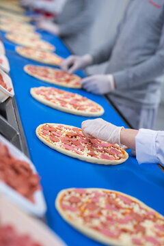 Workers Placing Toppings on Pizzas in Factory