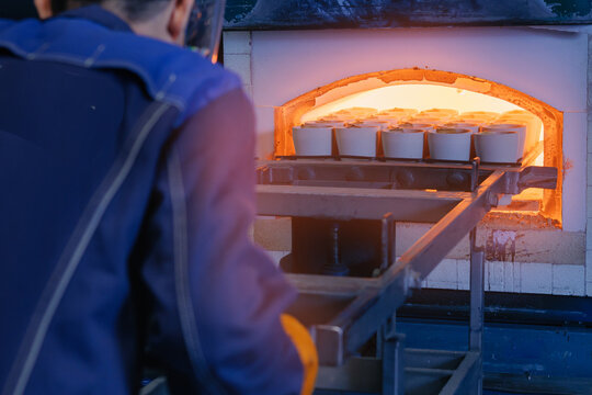 Worker loading ceramic pots with ore into glowing industrial kiln, mining factory