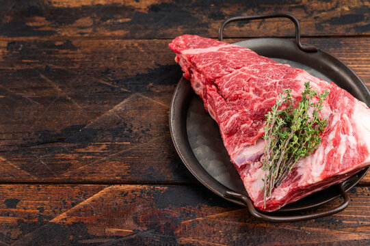 Raw marbled beef chuck meat in metal pan with garlic and thyme on rustic wooden background. Premium meat preparation with copy space.