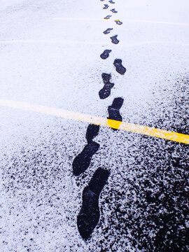 Footprints in the Snow Walking Across Parking Lot with Yellow Lines on Street