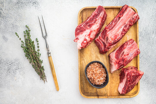 Raw beef short ribs chunks with rich meat texture, thyme and salt on tray. Light background with copy space for food design.