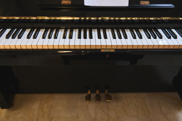 Close-up of upright piano keyboard and pedals in polished black finish © Taras Grebinets