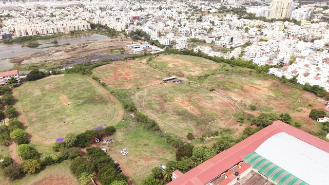 Five cricket grounds at a sports academy seen from above beside a growing city