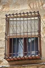 Obraz premium Traditional window with wrought iron security grille and wooden shutters on a weathered stone facade in Baeza, Andalusia, Spain