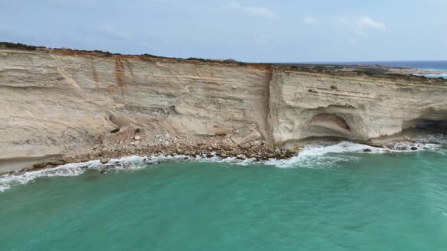 limestone sea cliff rockfall talus natural cave opening turquoise water aerial drone orbit malta coastline eroded rock strata coastal erosion rugged shoreline mediterranean sea cliff karst geology