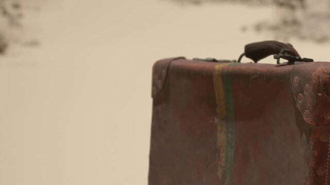 A suitcase is placed on a sandy surface in a natural setting. The area is dry and appears to be a remote location with no people nearby. The time of day is unclear.