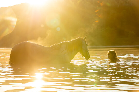 Frau badet mit Pferd im See