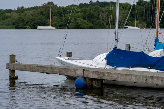 Sailing boat moored beside a pontoon on Wroxham Broad, Norfolk, with calm waters and a peaceful summer landscape.