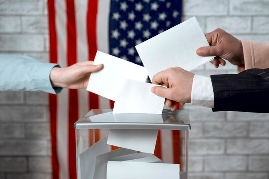 Multiple voters casting ballots into a ballot box with the US flag. American elections, democracy and voter participation.