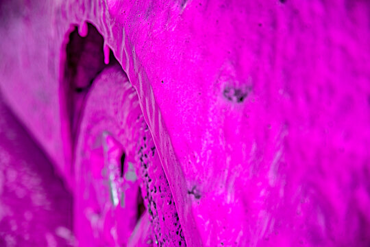 Car vehicle is coated in bright magenta soap pink foam during touchless pressure washing cleaning at a self-service car wash station.