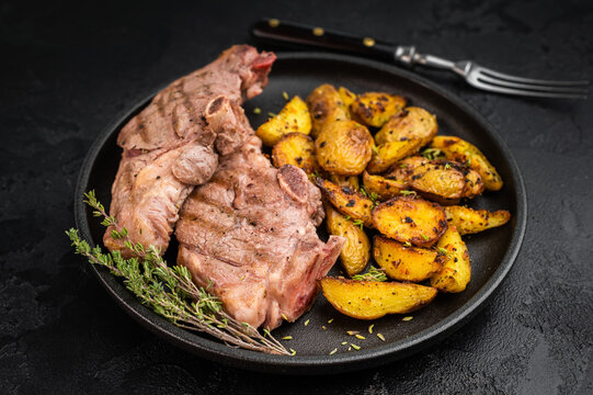 Roasted lamb rump steak with crispy golden potatoes served on dark plate, cooked sirloin saddle meat styled in rustic overhead composition.