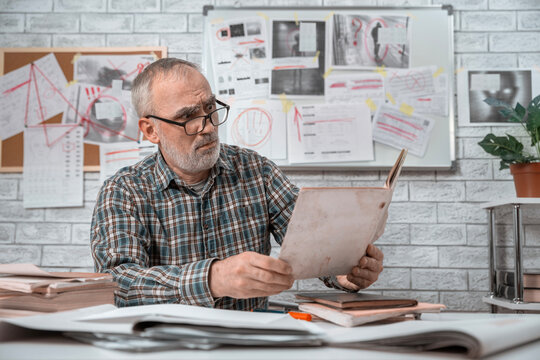 Older investigator reviewing case papers while working on an unsolved crime in a detective office