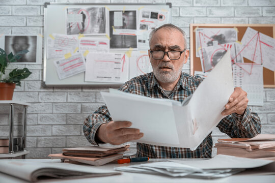 Senior criminal detective examining large case documents at a desk with an evidence board and investigation files in the background.