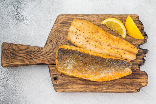 Crispy golden sea bass branzino fish fillet plated on wooden cutting board, overhead food photography with light background and space for text.