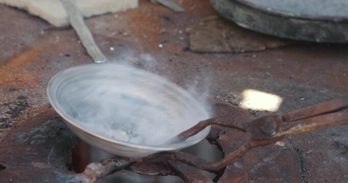 Coppersmith tinning and coating copper bowl over fire with tin and sal ammoniac in traditional workshop