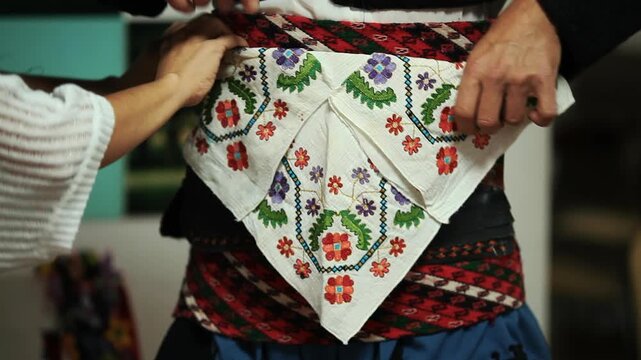 Dressing in traditional folk costume and tying hand embroidered floral sash to waist for cultural dance performance