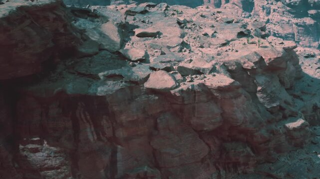 The scene shows rocky terrain with layered cliffs and shadows in a natural landscape. The sunlight creates depth on the rocks. The time is midday, and the area is dry.