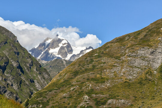 Majestic snow covered mountain glacier peak peaking from behind rugged alpine hills under a bright blue sky, La Thuile, Aosta Valley, Italy
