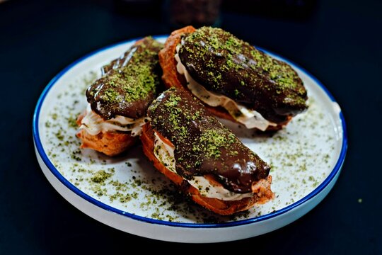 Chocolate Glazed Cream-Filled Choux Pastries Topped with Pistachio on a White Plate