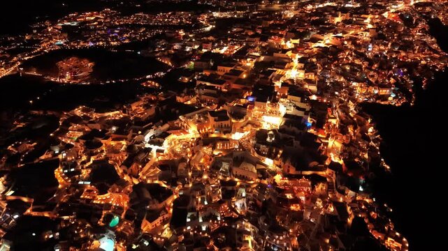 High angle night drone of Oia dense village layout with illuminated cave hotel pools in Santorini Greece