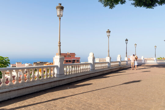 A young couple enjoys sea and town views from a scenic viewpoint terrace in the historic town of Icod de los Vinos, Spain, on the island of Tenerife, Canary Islands.