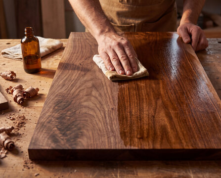 Hands apply tung oil to a walnut tabletop with raw and oiled grain side by side