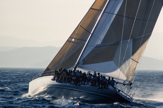 Modern racing yacht with full crew hiking out on heeled deck, vintage 35mm film scan. Teamwork, speed, intense regatta competition, nautical mastery concepts.