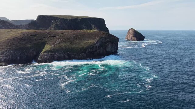 Smooth aerial drone approach from the side toward the headland Eire 63 Sign, at Portacloy, county Mayo, Ireland. A rugged headland surrounded by deep blue Atlantic water. Dramatic coastal landscape