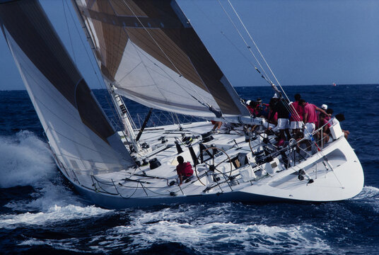 Stern perspective of racing yacht heeling steeply in rough seas with crew on rail, vintage 35mm film scan. Teamwork, precision navigation, high performance sailing.
